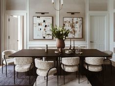 a dining room table with chairs and flowers in a vase on the top, surrounded by art