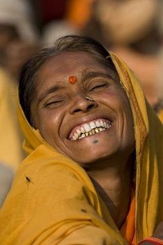 a smiling woman with her eyes closed wearing a yellow sari and orange nose ring