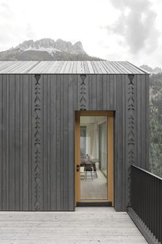 an open door on the side of a wooden building with mountains in the background,