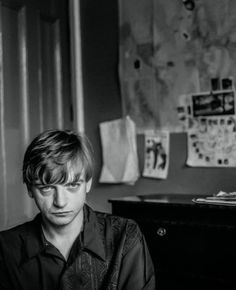 black and white photograph of a young man sitting in front of a desk with papers on it