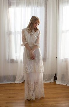 a woman standing in front of a window wearing a long white dress with sheer sleeves