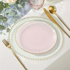 a table setting with pink and gold plates, silverware and flowers on the table