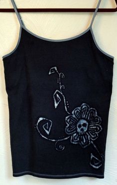 a black tank top with a flower embroidered on the front and side, hanging from a metal hook