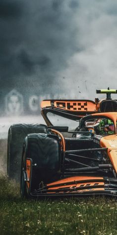 an orange race car is driving on the grass in front of some dark storm clouds