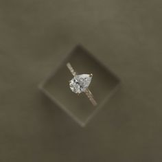 an engagement ring with a pear shaped diamond in the center on a square surface, viewed from above