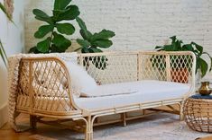 a wicker couch with white cushions in front of a brick wall and potted plants