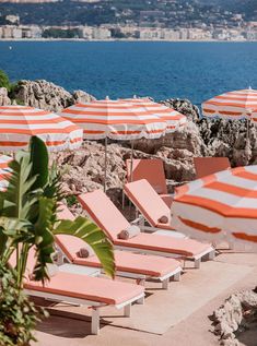 lounge chairs and umbrellas are lined up on the beach near the water's edge