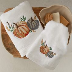 two white towels with embroidered pumpkins and leaves on them are sitting on a wooden tray