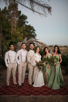 a group of people standing next to each other on a red rug in front of trees