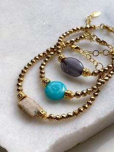 JAYA Bracelet Material: Jade, African Opal, Agate, Hematite, Gold plated brass, Steel parts Dimensions: 17cm +5cm extender chain / 6.7in +2in extender chain AGATE-Grey JADE-Turquoise OPAL-Beige ⛦Natural Semi-precious Stones ⛦Adjustable Length ⛦Delivered in a fabric pouch ⛦Handcrafted in our workshop in Athens and Limnos Island ⛦Follow us on instagram: @puregreekshop All PURE GREEK Jewels are inspired from the ancient greek arts, folklore traditions and world cultures. Our jewelry are handmade with love and imagination so you can enjoy unique creations.  I use mineral and semi-precious stones, crystals, real pearls, gold plated brass metal, wooden elements, greek and oriental charms, pompons and feathers. I only use high quality materials that guarantee great comfort and longevity to our je Semiprecious Stone Bracelet, Gold Beaded Bracelets With Natural Stones As A Gift, Turquoise Bracelet With Polished Beads As Gift, Bohemian Gold Bracelets With Gemstone, Gold Agate Beaded Bracelets With Gemstones, Bohemian Crystal Bracelet With Polished Beads As Gift, Turquoise Bangle Beaded Bracelets With Natural Stones, Gold Beaded Gemstone Bracelets For Jewelry Making, Gold Bracelets With Agate And Natural Stones