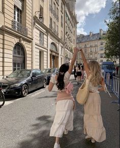 two women walking down the street with their arms in the air