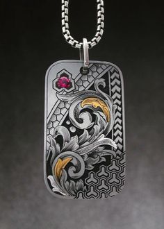 a dog tag with an intricate design and a red stone in the center on a chain