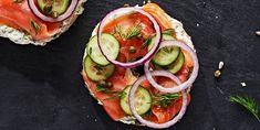 two sandwiches with cucumbers, tomatoes and onions on them are sitting on a black surface