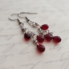 Bloodstone Red Czech Glass Cluster Drop Earrings in Antiqued Silver EARRINGS ONLY Such a rich gothic garnet or bloodstone red! Please note: Bringing them into light draws out the red, otherwise they can almost appear black.  I wrapped garnet Czech glass teardrop beads in titanium wire and minimally suspended three from a length of antiqued silver chain to form a delightful cluster dangle. Earrings fall from your choice earwires.   Earrings can appear almost black in the shadows but light brings out the glorious shades of red.  For clarification, these are not gemstones but Czech glass.  Want a full ensemble?? Add on the pendant in the same bloodstone red/garnet Czech glass as seen in a few of these images. https://www.etsy.com/listing/1157131359/garnet-red-cluster-pendant-necklace REPEAT C Red Wire Wrapped Dangle Earrings, Red Teardrop Chandelier Earrings, Red Teardrop Chandelier Earrings With Ear Wire, Red Gothic Earrings For Pierced Ears, Red Nickel-free Chandelier Earrings As Gift, Red Wire Wrapped Metal Earrings, Gothic Red Nickel-free Earrings, Antique Silver Earrings, Garnet Red