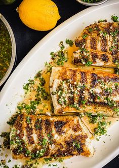 grilled fish on a white platter with lemons and seasoning