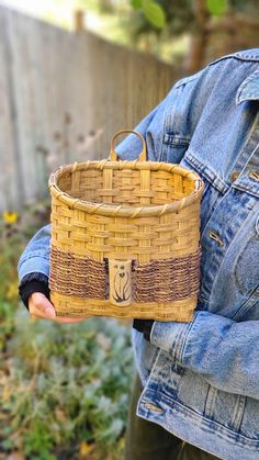 a person holding a woven basket in their left hand and wearing a denim jacket on the other