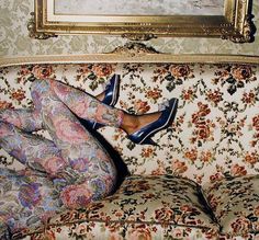 a woman laying on top of a floral couch next to a framed painting above her head