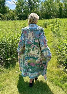 a woman is walking in the grass with her back turned to the camera and wearing a colorful coat