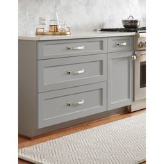 a kitchen with grey cabinets and white counter tops, an oven and stove top in the background