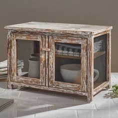 an old wooden cabinet with glass doors and plates in the bottom drawer, sitting on a white tiled floor