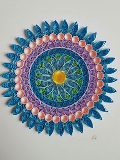 a paper quilled artwork with blue, pink and orange flowers in the center on a white background