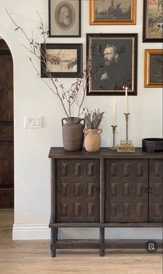 a vase with some flowers on top of a wooden cabinet next to pictures and candles