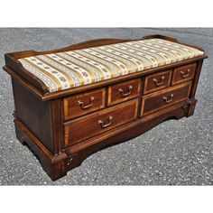 an antique wooden bench with striped fabric on it's seat and back rests on the pavement