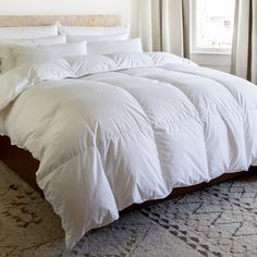 a large white bed sitting in a bedroom next to a window with drapes on the windowsill