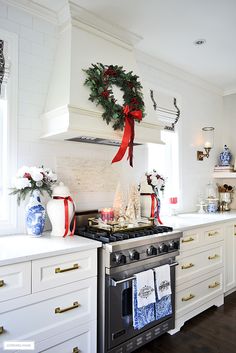 a kitchen decorated for christmas with wreaths on the stove and garland hanging over the range