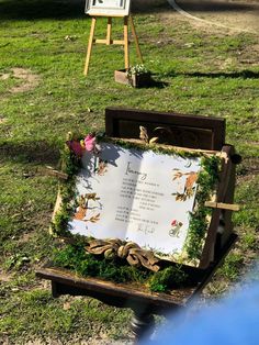 an open book sitting on top of a wooden bench in the grass next to easels