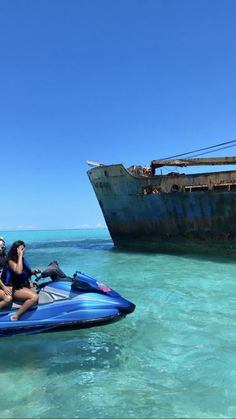 two people on a jet ski in the water near an old ship and another boat