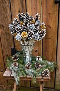 a glass vase filled with pine cones sitting on top of a wooden table next to a fence