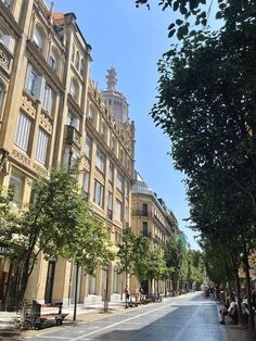 an empty street lined with tall buildings and lots of trees on the side of it