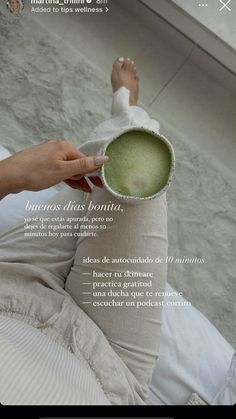 a woman laying on top of a bed next to a white pillow and cup filled with green liquid