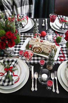 the table is set for christmas dinner with black and white checkered cloths, red roses, silverware, candlesticks, and candy cane