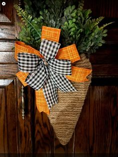 an orange and black bow is hanging on the front door with greenery in it