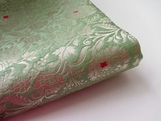 a green and pink brocaded fabric on a white tablecloth with red dots