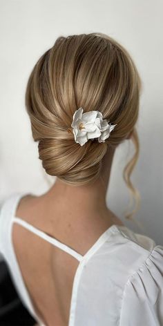 a woman with blonde hair and a flower in her hair is wearing a white top