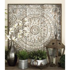 an ornate metal wall panel with flowers in vases on a table next to two lanterns