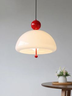 a red and white light hanging from a ceiling fixture over a table with a vase on it