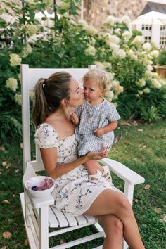 a woman sitting in a white chair holding a small child and kissing her cheek on the cheek