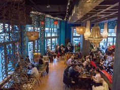 people sitting at tables in a restaurant with large windows and chandeliers hanging from the ceiling