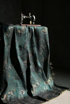 an old sewing machine sitting on top of a table covered by a green cloth with gold flecks