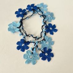 a blue and white crocheted flower necklace on a white table with a black cord