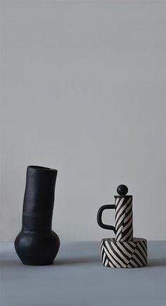 two black and white vases sitting next to each other on a table with a gray wall in the background