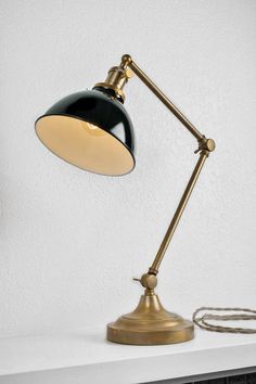 a black and gold desk lamp sitting on top of a white shelf next to a wire