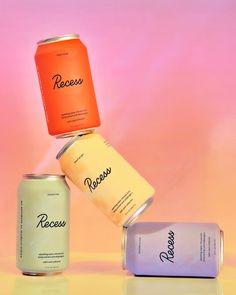 three cans of soda sitting on top of each other in front of a pink background