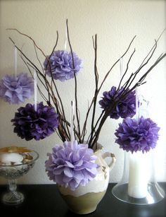 purple flowers in a white vase on a black table next to a glass bowl and candle