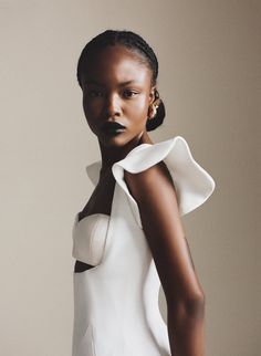 a woman in a white dress with black lipstick on her face and hands behind her back