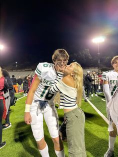 two football players kissing each other on the sidelines at night with fans in the background